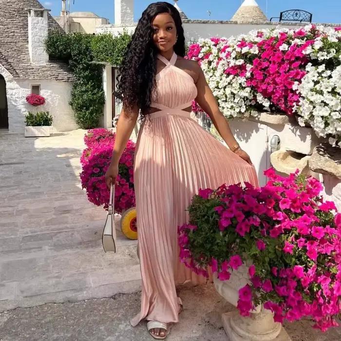 Robe longue plissée rose poudré en satin pour femme, style africain élégant, avec découpes à la taille, sans manches, pour soirée ou événement.