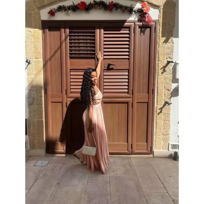 Robe longue plissée rose poudré en satin pour femme, style africain élégant, avec découpes à la taille, sans manches, pour soirée ou événement.